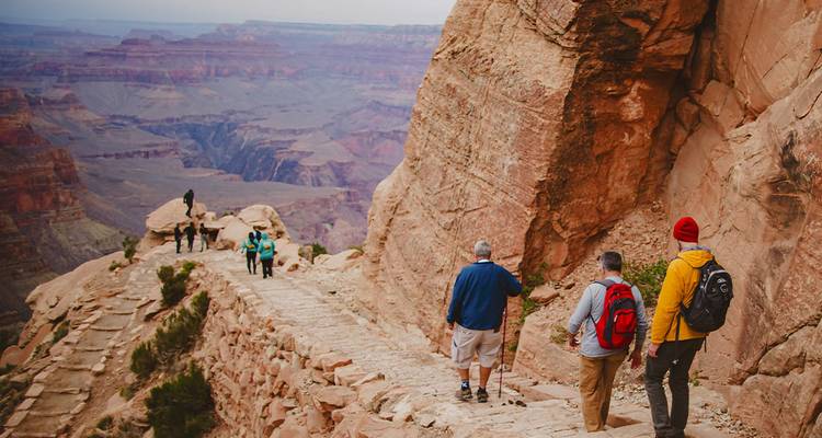 Hikers walking along a trail with the Grand Canyon in the background.