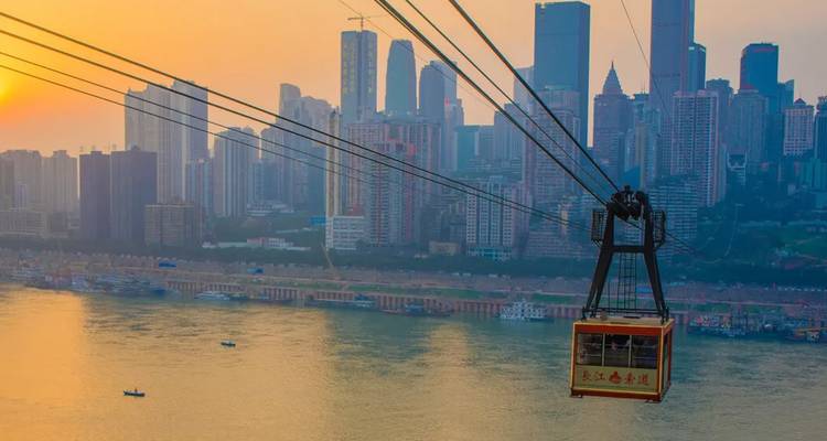 Cable car over a river with cityscape view at sunset.