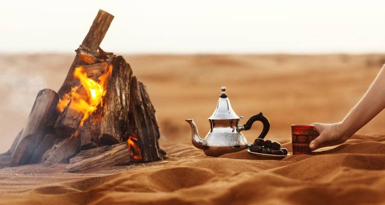 Traditional tea set and a campfire in a desert landscape.