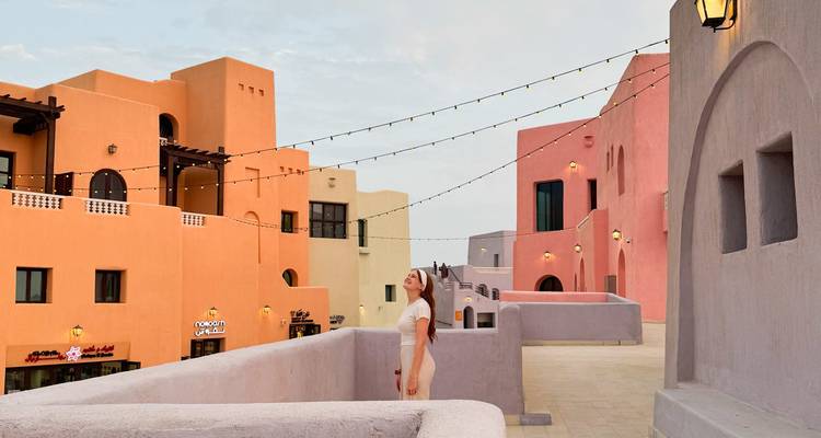 Woman standing among colorful, traditional buildings under a cloudy sky.