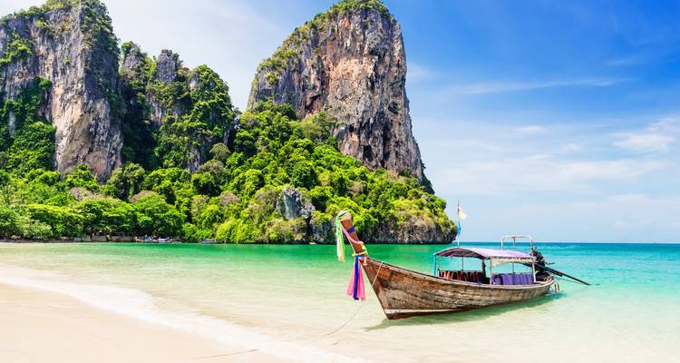 Bateau à longue queue traditionnel sur une plage tropicale avec des falaises calcaires.