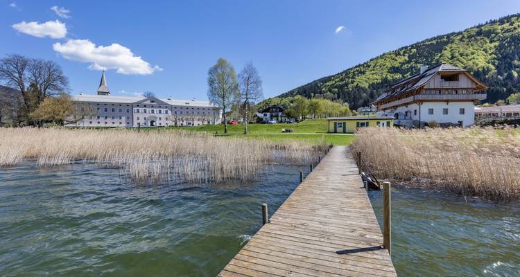 Muelle en un lago con juncos y montañas al fondo.