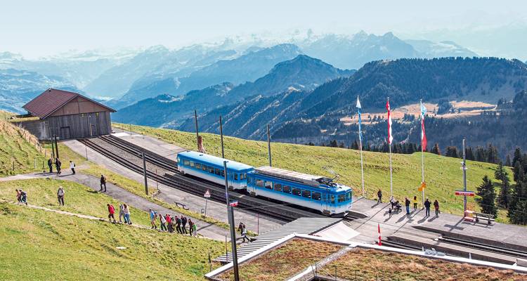 Ein Bahnhof in den Bergen mit Menschen, die entlang des Bahnsteigs gehen.