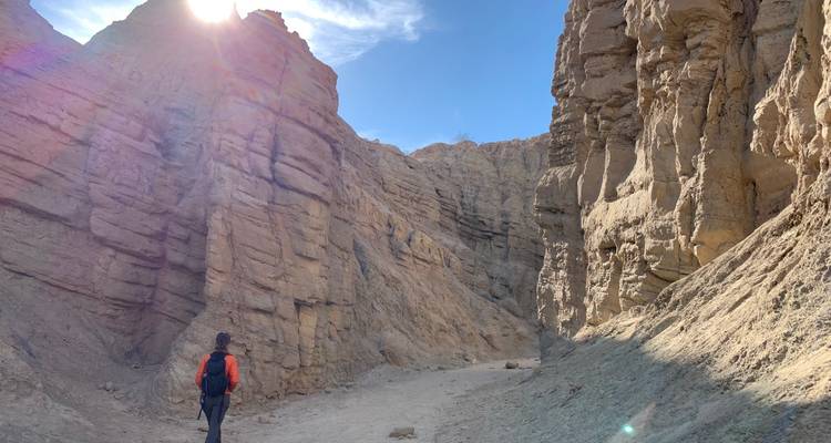 Person walking in a wide canyon with sunlight peeking over the rocks.