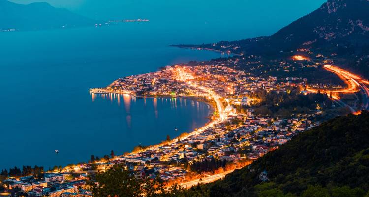 Vue nocturne d'une ville côtière avec des bâtiments illuminés.