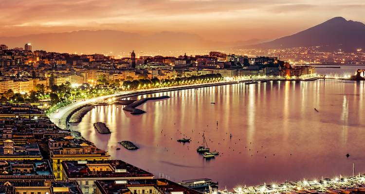 Avondzicht van een stad aan het water met een berg op de achtergrond.