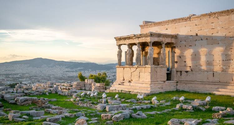 Ruines historiques avec des statues surplombant une ville au crépuscule.