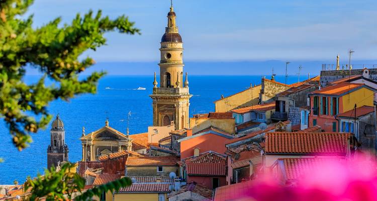 View of colorful coastal town with a church tower and the sea in the background.