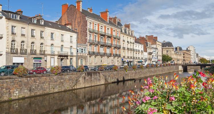 Row of historic buildings along a river with vibrant flowers.