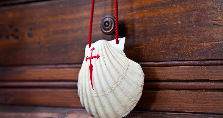 Concha de vieira con una cruz roja colgando de madera, simbolizando el Camino de Santiago.