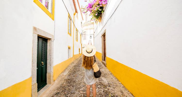 A person walking down a narrow cobbled street with white and yellow buildings.