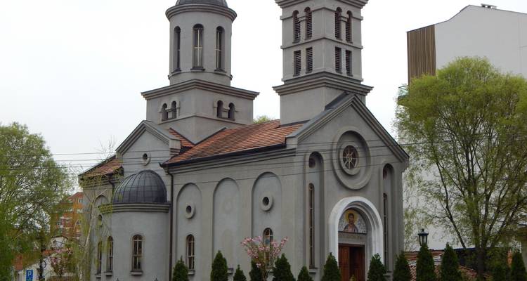 Graue Kirche mit zwei Glockentürmen in städtischer Umgebung.