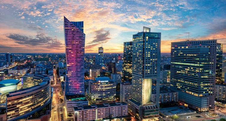 City skyline at sunset with modern skyscrapers and colorful lights.