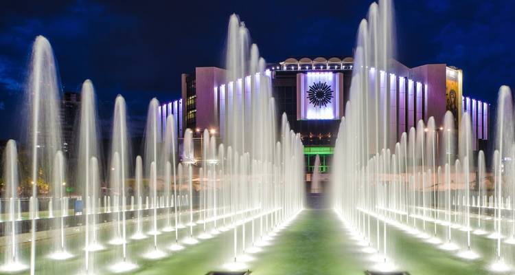 Fontaines illuminées et un bâtiment moderne la nuit.