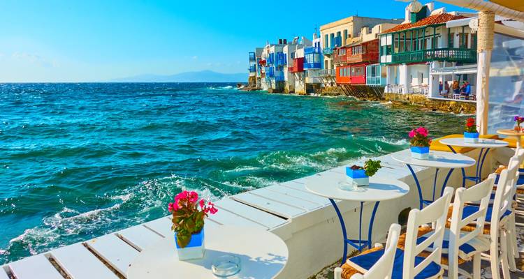 Café en bord de mer avec tables et chaises donnant sur une mer d'un bleu éclatant.