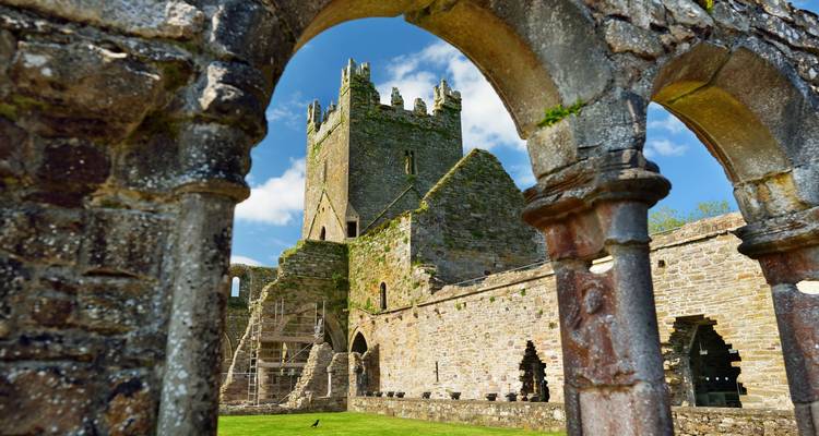 Vue d'une ruine de château encadrée par des arches dans un environnement ensoleillé.