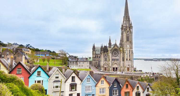 Maisons colorées au bord d'une rivière avec une grande église en arrière-plan.