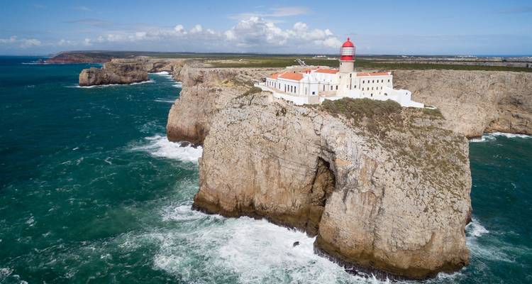Phare sur des falaises avec des vagues qui se brisent en contrebas au coucher du soleil.