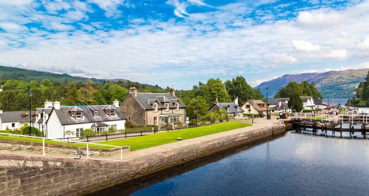 Charmant village au bord d'un cours d'eau avec des montagnes en arrière-plan.