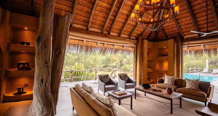 Open lounge area in a thatched roof building overlooking a pool.