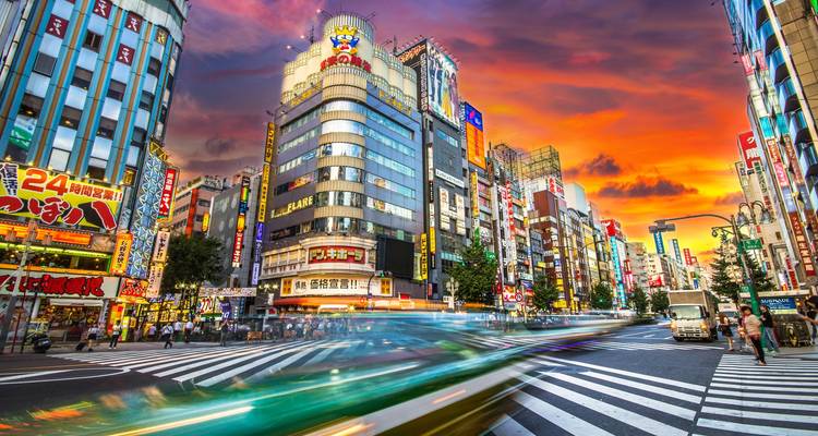 Intersection animée à Tokyo avec de grands bâtiments and un coucher de soleil vibrant.