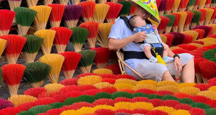 Personne tenant un bébé entourée de bâtons d'encens colorés.