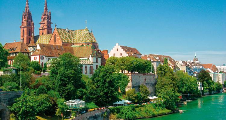 Flussblick mit einer großen Kathedrale und historischen Gebäuden entlang eines grünen Flussufers.