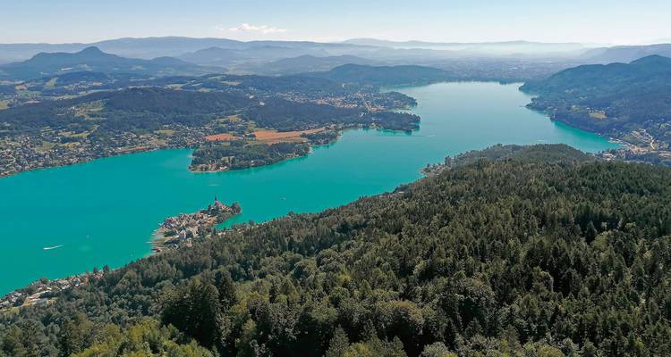 Panoramic view of a lake surrounded by forests and mountains.