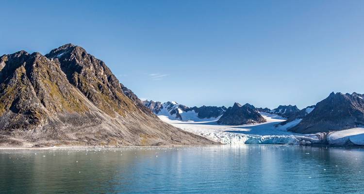 Montagnes enneigées avec un glacier s'étendant dans une mer calme.