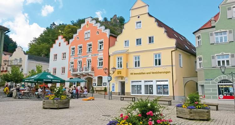 Charmanter bayerischer Marktplatz mit pastellfarbenen Giebelhäusern, Café-Schirmen und Blumenkästen