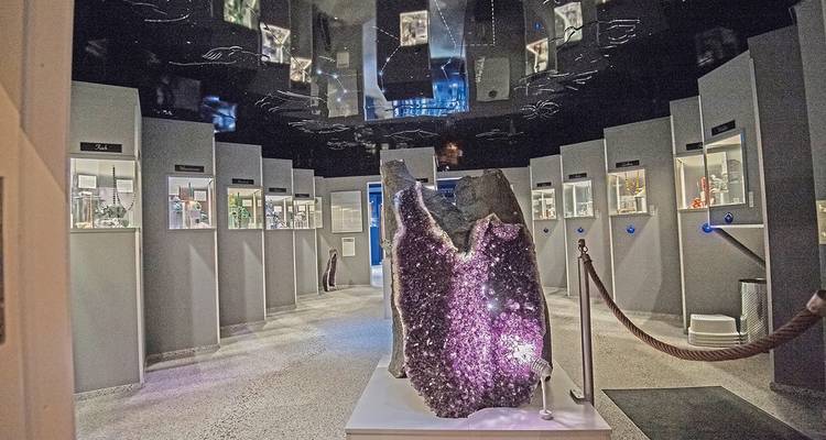 Museumsgalerie mit einer großen Amethystdruse, umgeben von beleuchteten Mineralienausstellungen