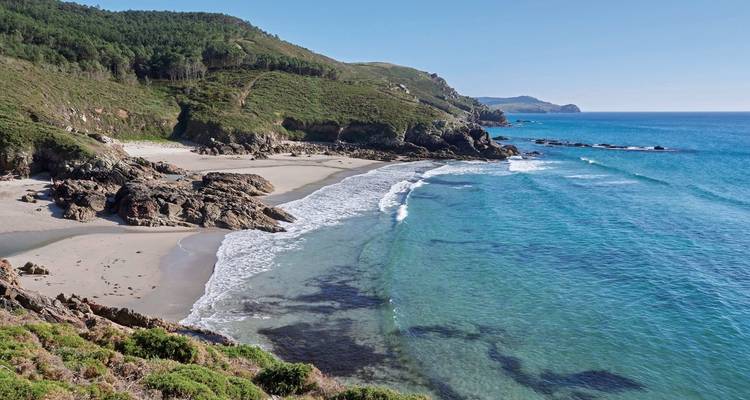 Malerischer Strand mit Wellen und grünen Hügeln.