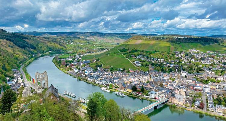 Paysage urbain avec une rivière qui traverse une vallée entourée de collines et un château au sommet de la colline.