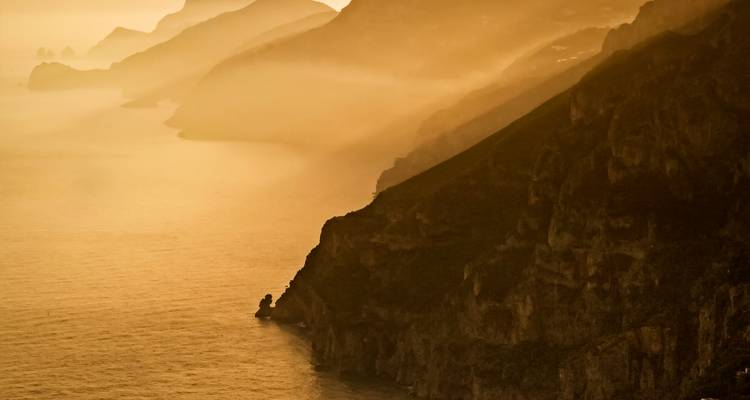 Vista costera pintoresca con acantilados y una puesta de sol brumosa.