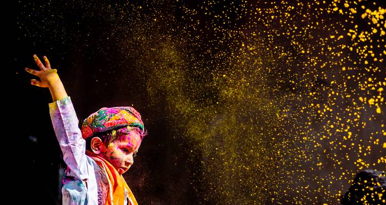 Kind met kleurrijke poeders in de lucht die een festival viert.