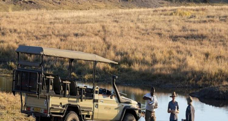 Safari vehicle with people near a water body.