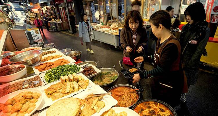 Vendeur de nourriture de rue préparant de la nourriture dans un marché animé avec des gens autour.