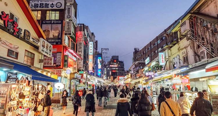 Vue de la ville le soir avec des lumières vives et des foules dans la rue.