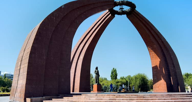 Une arche commémorative en pierre rouge saisissante dans un cadre de parc.