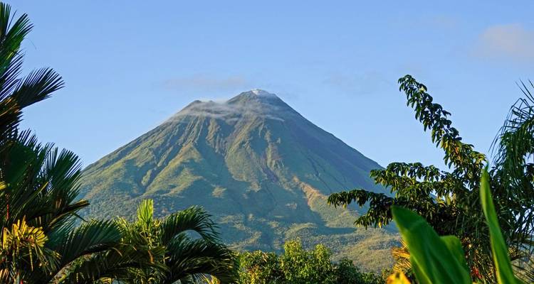 A volcano with a lush green base under a clear blue sky.