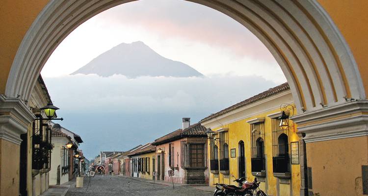 Arche historique encadrant une vue de rue avec un volcan en arrière-plan.