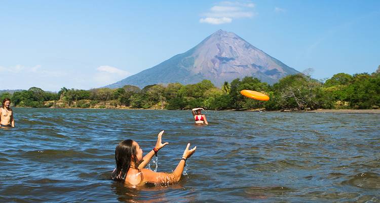 Des gens qui nagent et jouent dans l'eau avec une montagne volcanique en arrière-plan.