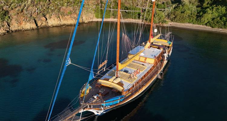 Un grand voilier amarré dans une baie calme entourée de verdure.