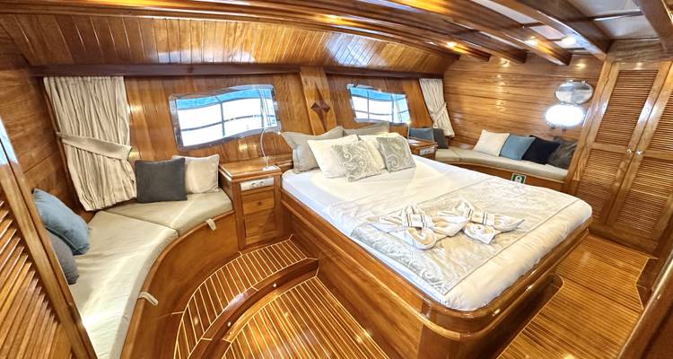 Habitación de camarote de madera en un barco con cama y área de descanso.