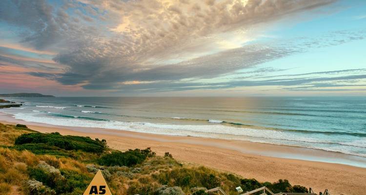 Una vista panorámica de una playa y océano durante el atardecer con olas y nubes en el cielo.