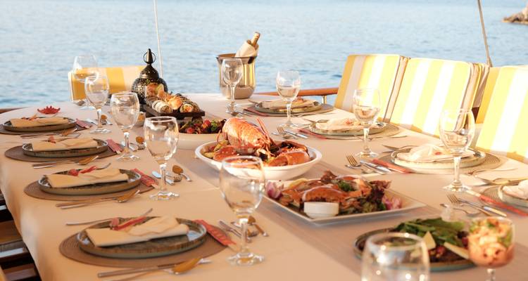 Table à manger dressée avec nourriture et boissons dans un cadre nautique.