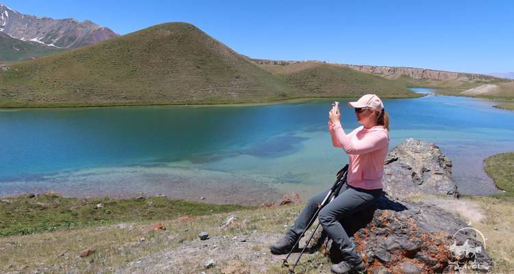 Personne assise sur un rocher prenant une photo d'un lac entouré de collines.