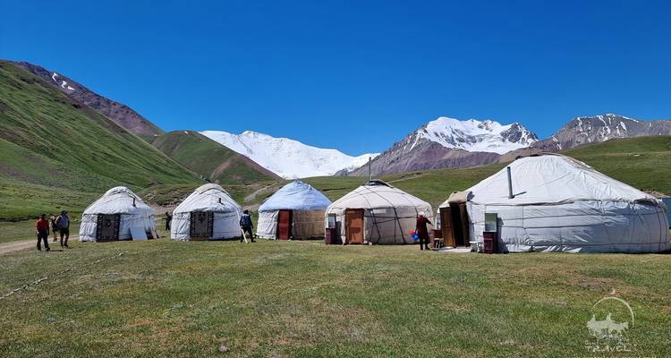 Une rangée de yourtes avec des montagnes enneigées en arrière-plan.