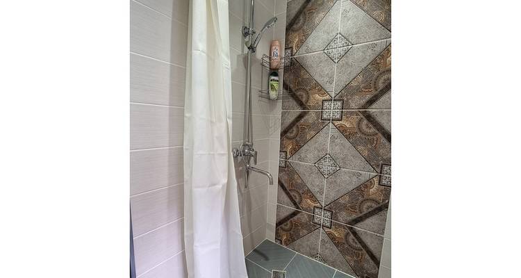 Une douche avec des carreaux décoratifs et un rideau.