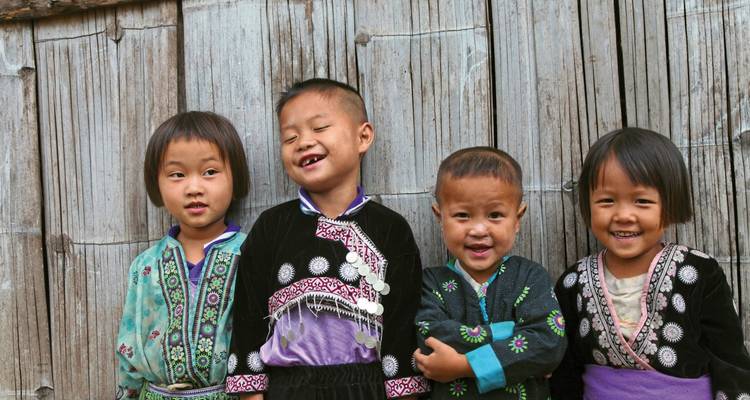 Children in traditional attire posing against a wooden wall.